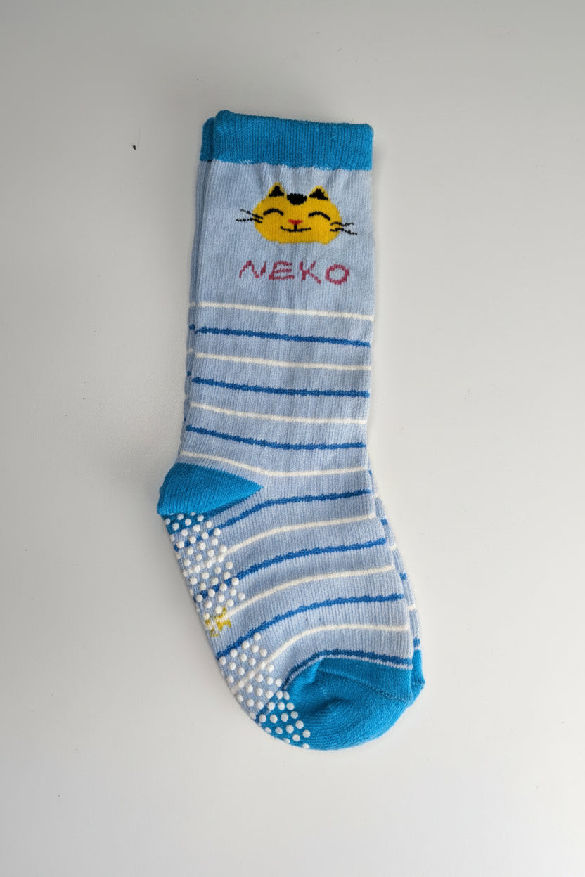 A single baby sock with blue and white stripes, a blue toe and heel, white grip dots on the sole, and a yellow cartoon cat face with the text 'NEKO' on the side, laid flat on a light gray background.